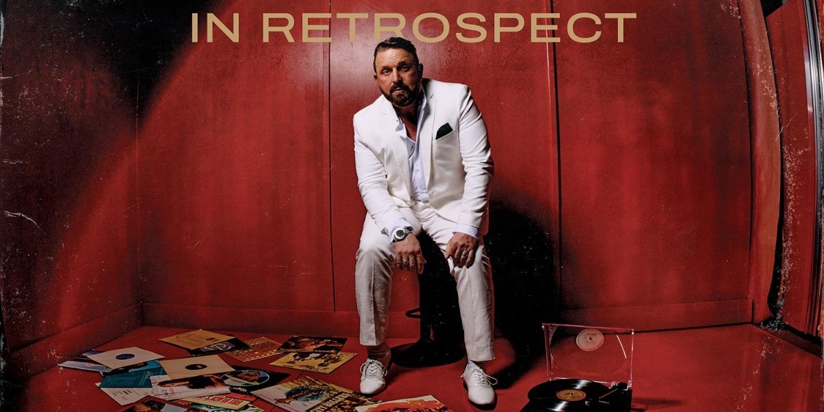 Johnny Reid's official In Retrospect album cover, showing the singer seated beside vinyl records