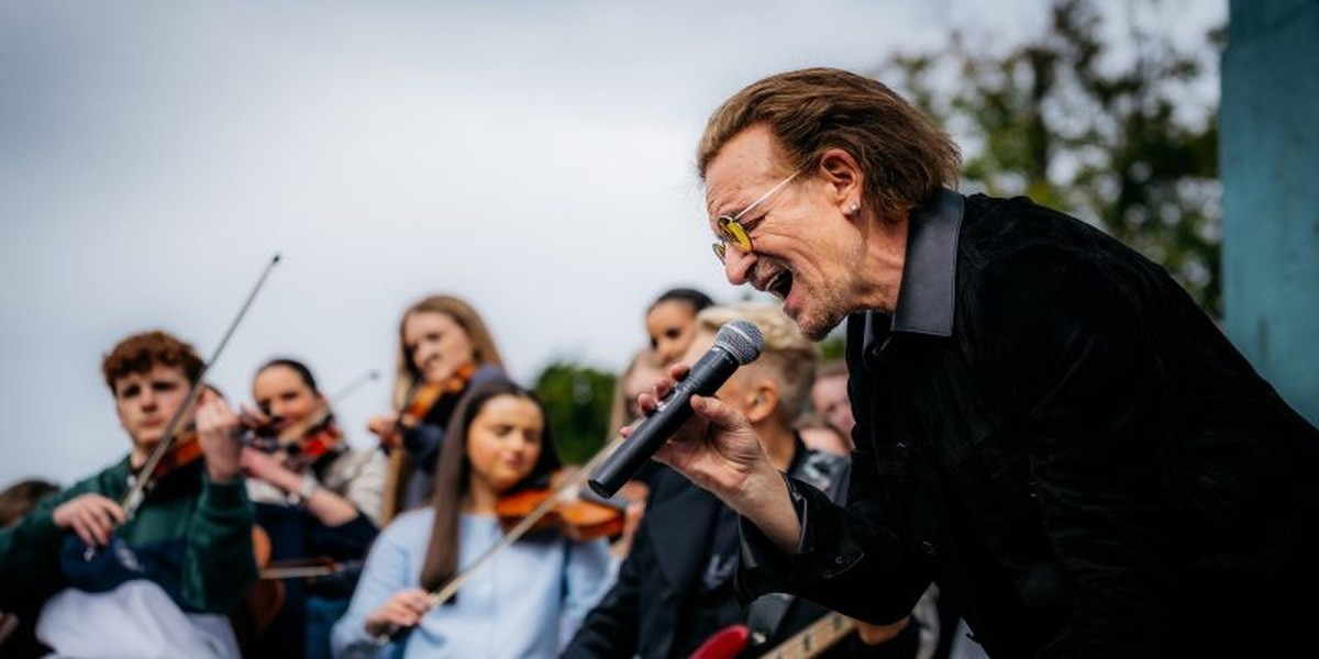 Bono sings into a microphone with musicians behind him at Mount Temple in Dublin.