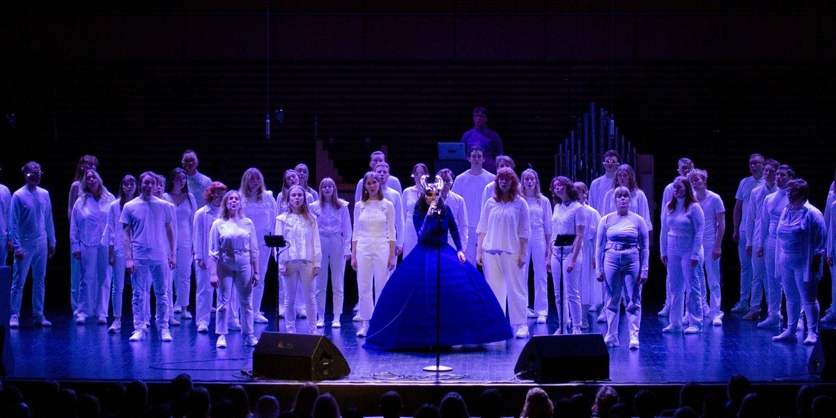Björk in a blue dress performs in front of the Hamrahlíð Choir at Harpa.